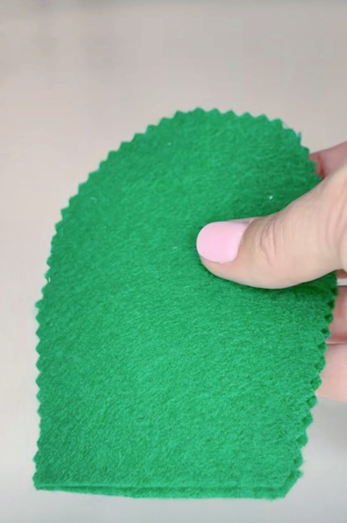 Image contains Amy’s hand holding two cut pieces of green felt.