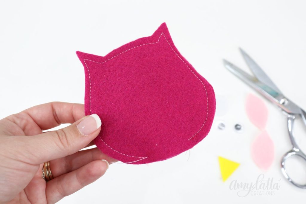 Image contains Amy’s hand holding two pink felt owl body pieces sewn together around the outside edges, with an opening at the bottom.
