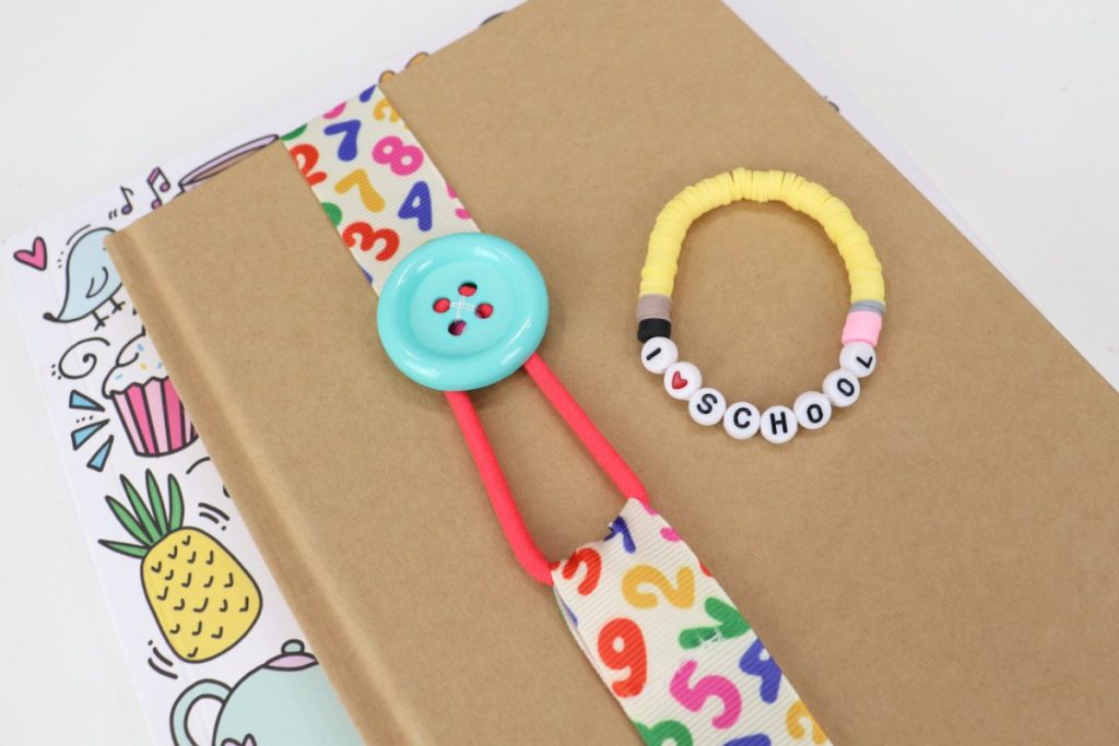 Image contains a brown journal with a  ribbon bookmark wrapped around it. The journal is sitting on top of a copy of the book Doodle Everything, and there is a yellow beaded bracelet on top of the journal.