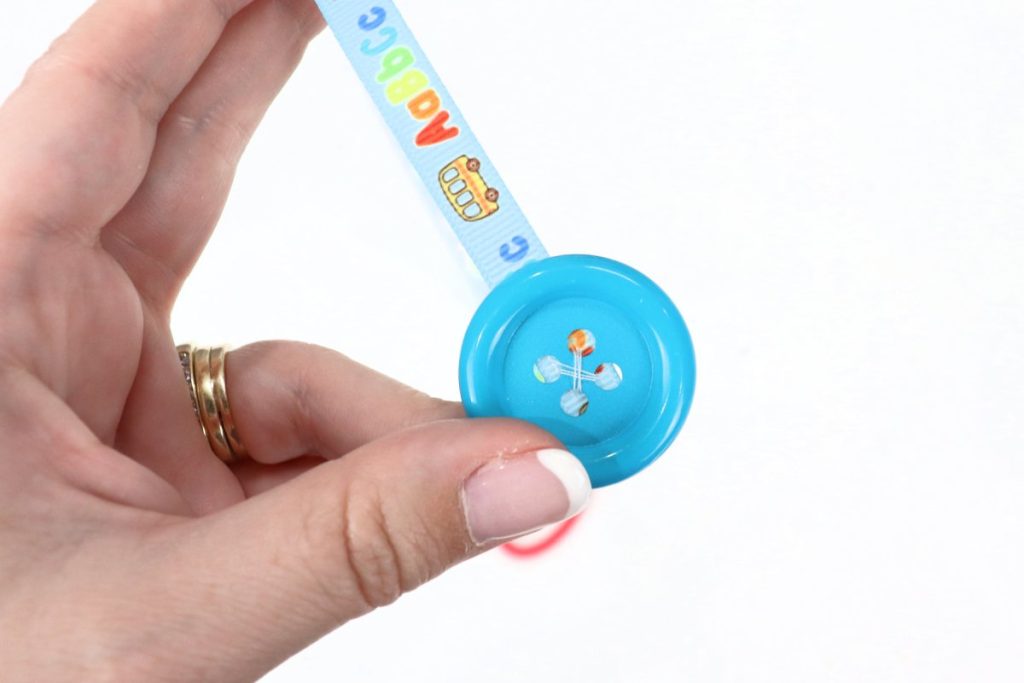 Image contains Amy’s hand holding a piece of blue ribbon with a large teal button on the end.