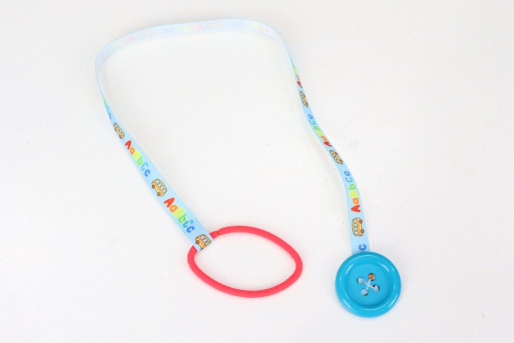 Image contains a piece of blue ribbon with a teal button on one end and a red hair tie on the other.
