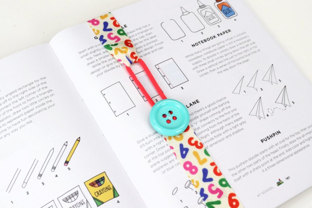 Image contains an open copy of the book Doodle Everything, with a ribbon bookmark wrapped around it.