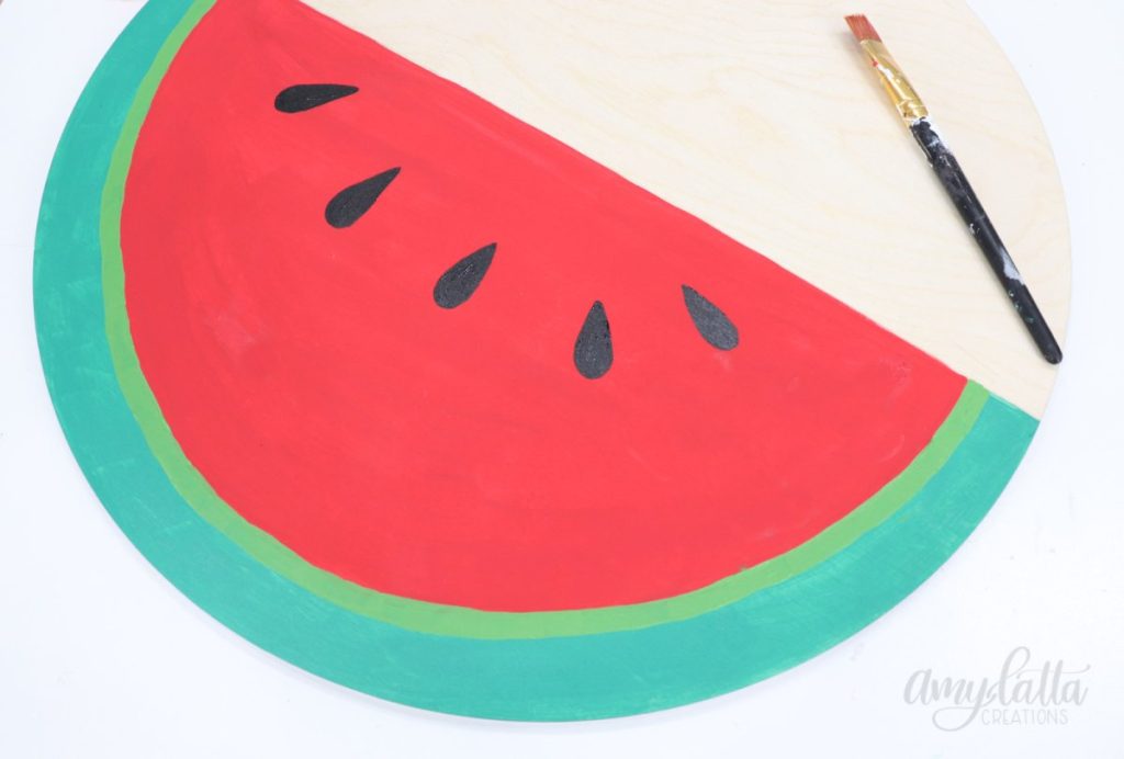 Image contains a large wooden circle with the bottom half painted to look like a watermelon. 
