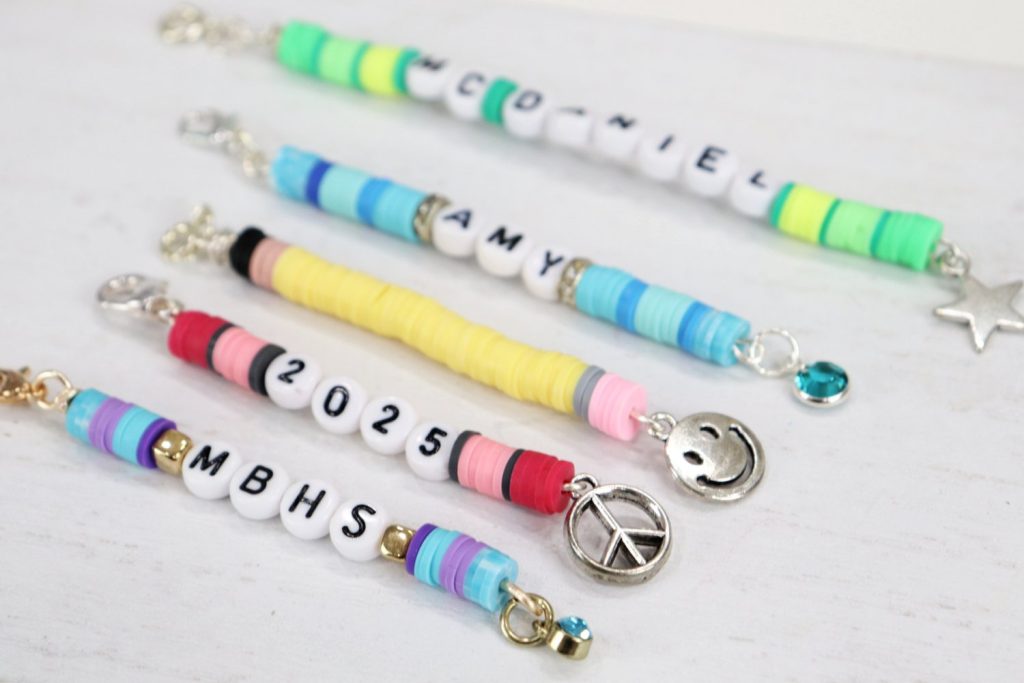 Image contains five beaded backpack charms made from various colors of clay beads, letter and number beads, and dangling charms.