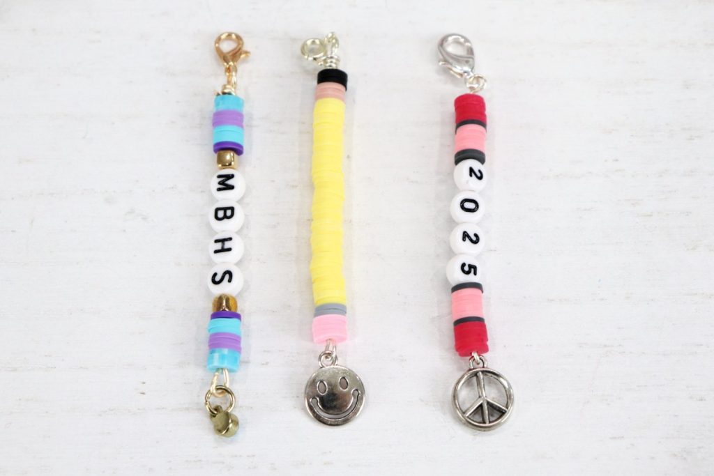 Image contains three backpack charms made from clay beads, letter and number beads, and dangling silver charms.