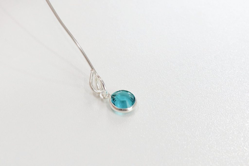 Image contains a teal gem charm attached to a silver wire loop.