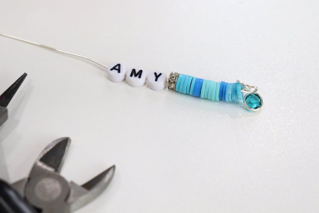 Image contains a piece of silver wire with blue and teal clay beads and letter beads spelling the name, “AMY."