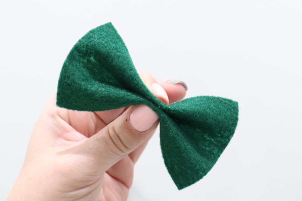 Image contains Amy’s hand holding a green felt rectangle pinched in the center to form a bow.