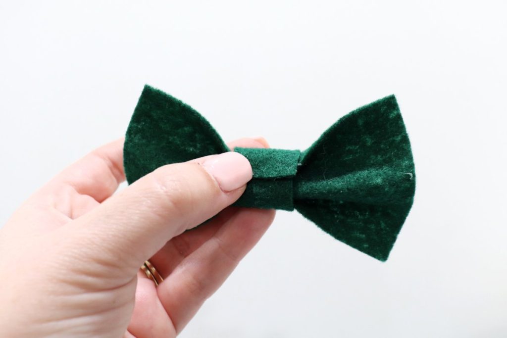 Image contains Amy’s hand holding a green felt bow with the back side in view.