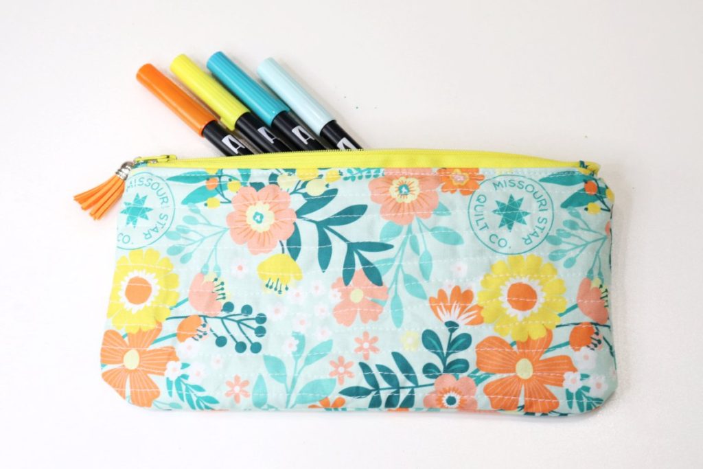 Image contains a teal, orange, and yellow floral pencil pouch with four markers peeking out of it on a white background.