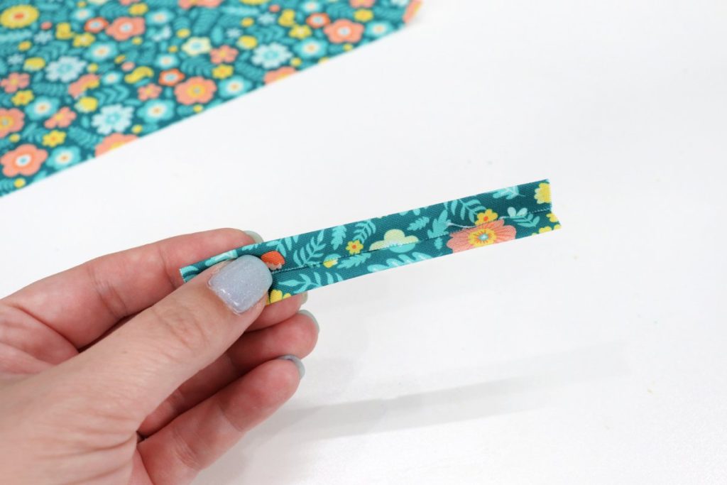 Image contains Amy’s hand holding a piece of fabric that has been folded to create a bias tape strip.