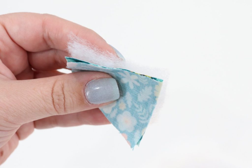 Image contains Amy’s hand holding two pieces of teal fabric and a piece of batting.