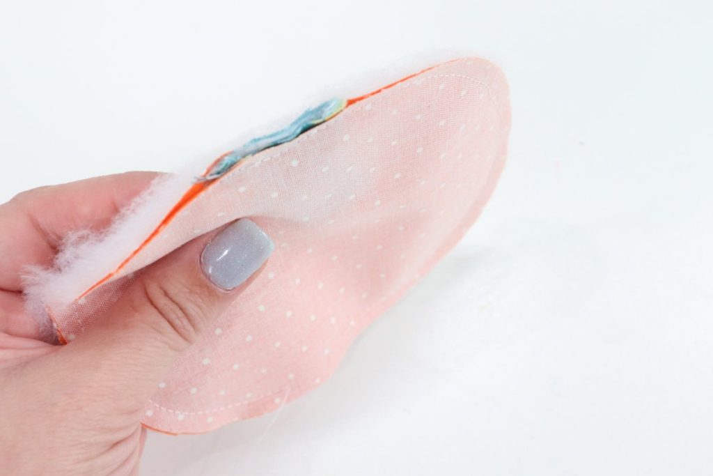Image contains Amy’s hand holding a layer of batting and two layers of orange fabric with the stem piece in between.