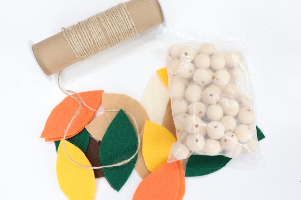 Image contains a pile of felt leaves, a bag of wooden beads, and a roll of twine.