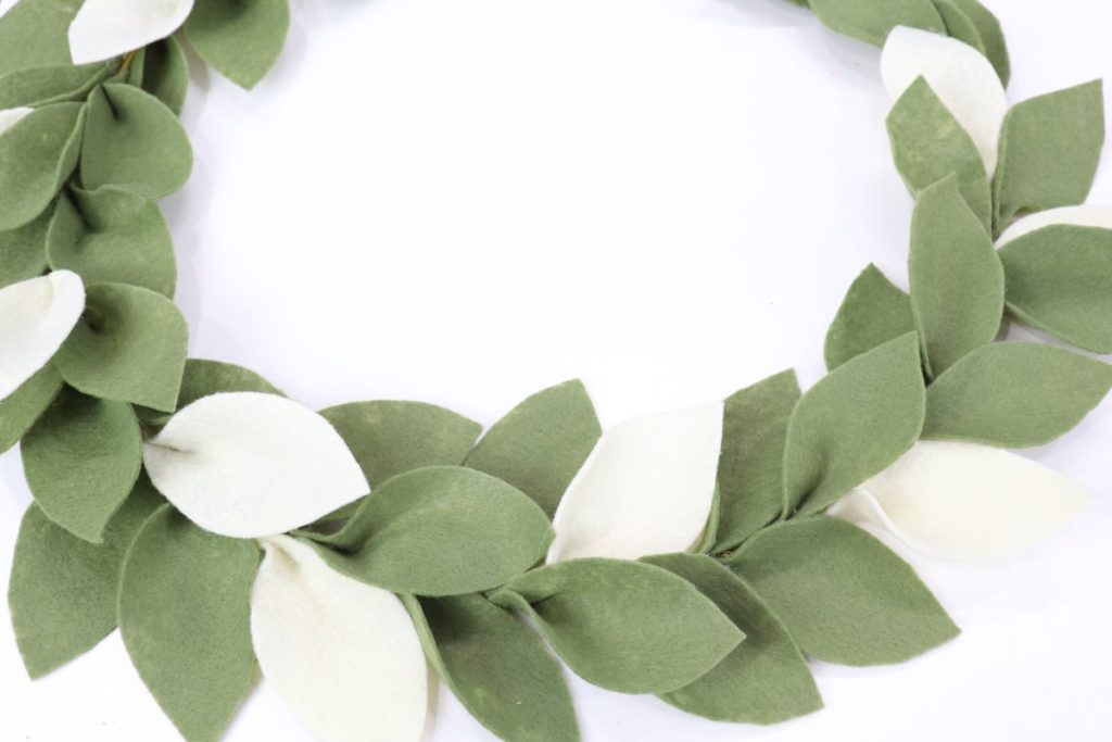Image contains a wreath made of green and cream felt leaves.