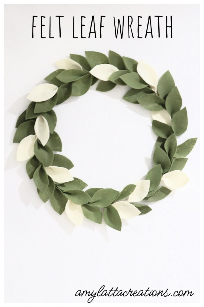 Image contains a wreath made of green and cream colored felt leaves on a white wall.