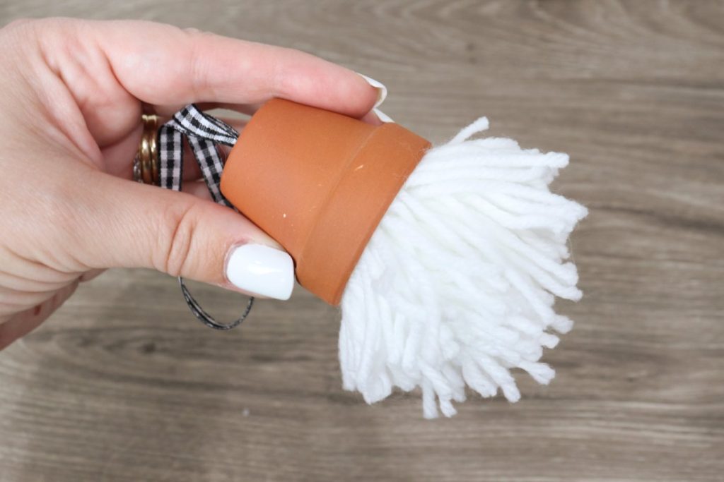 Image contains Amy’s hand holding a small terracotta pot with a black and white checkered ribbon through the bottom and a white pom pom glued inside.