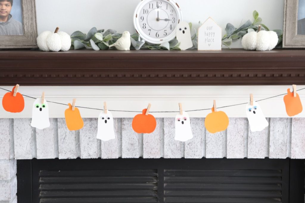 Image contains a white fireplace with a brown mantel, decorated with the finished Boo Garland.