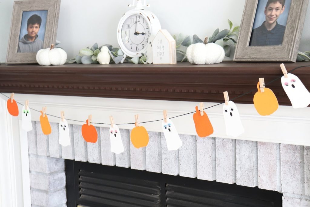Image contains a white fireplace with a dark brown mantel decorated with the finished Boo Garland.