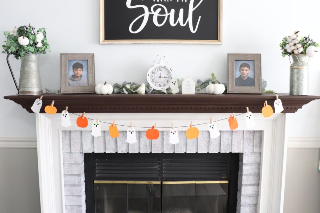 Image contains a white fireplace with a dark brown mantel. The front of the fireplace is decorated with the finished Boo garland.