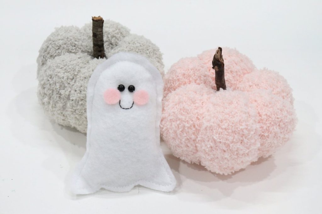 Image contains two homemade sock pumpkins, one beige and one peach, with small a felt ghost plush.