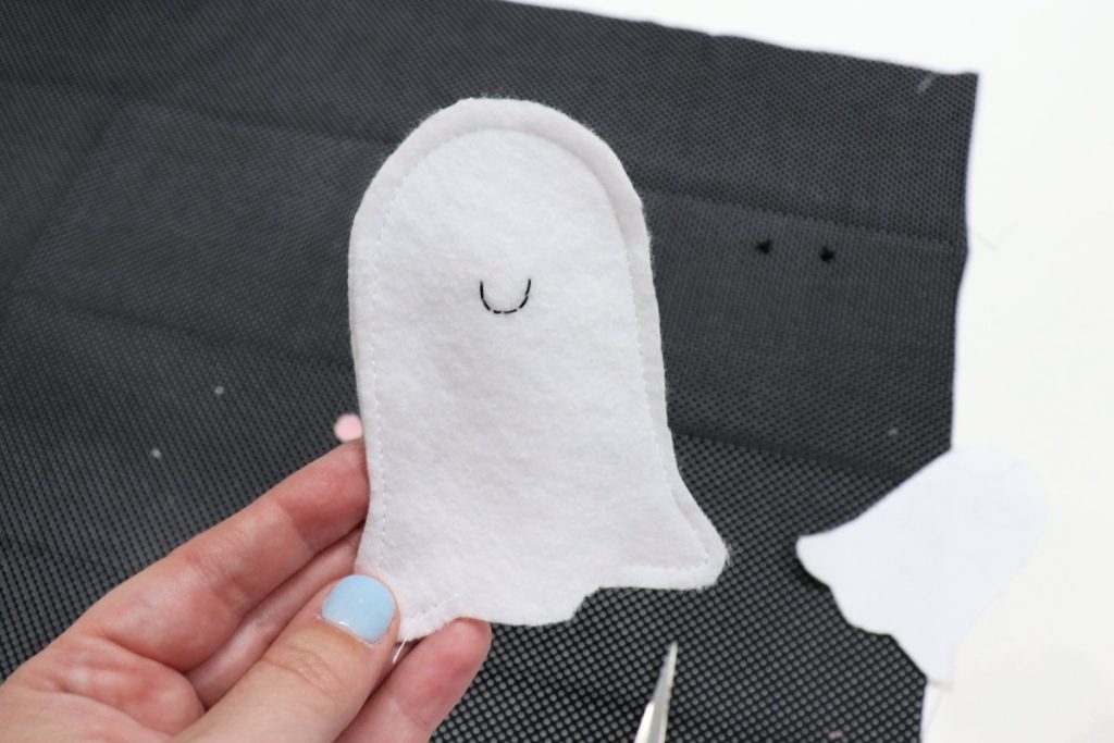 Image contains Amy’s hand holding a felt ghost that is stitched around the outside edges with an opening in the bottom.