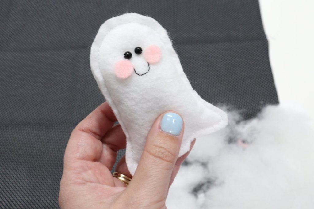 Image contains Amy’s hand holding a felt ghost plush with small bead eyes, a smile, and rosy cheeks.