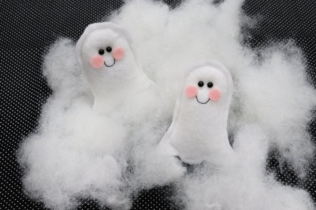 Image contains two felt ghosts surrounded by a cloud of Poly-Fil on a black background.