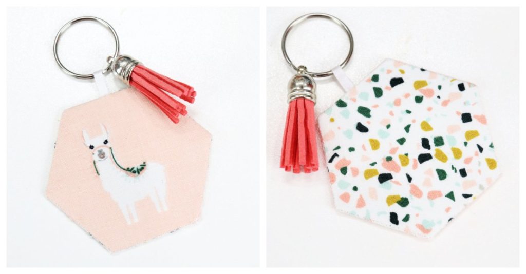 Image contains the front and back views of a fabric covered keychain. The front view features a llama on a blush background with a pink tassel, and the back contains a multicolor terracotta print with a pink tassel.