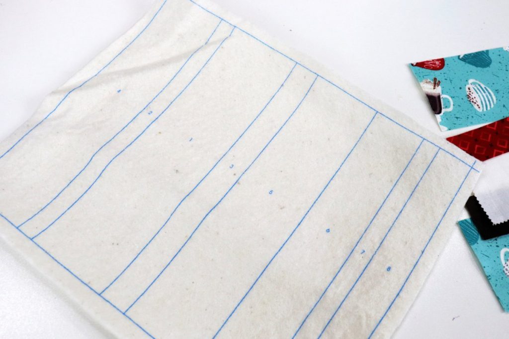 Image contains a piece of batting printed with numbered rectangle sections. Assorted fabric scraps sit off to the side.