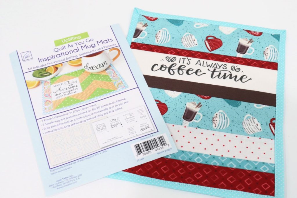 Image contains a quilted mug mat in teal, red, brown, and white fabrics with the words, “it’s always coffee time.” The packaging for the quilt as you go project sits on top.