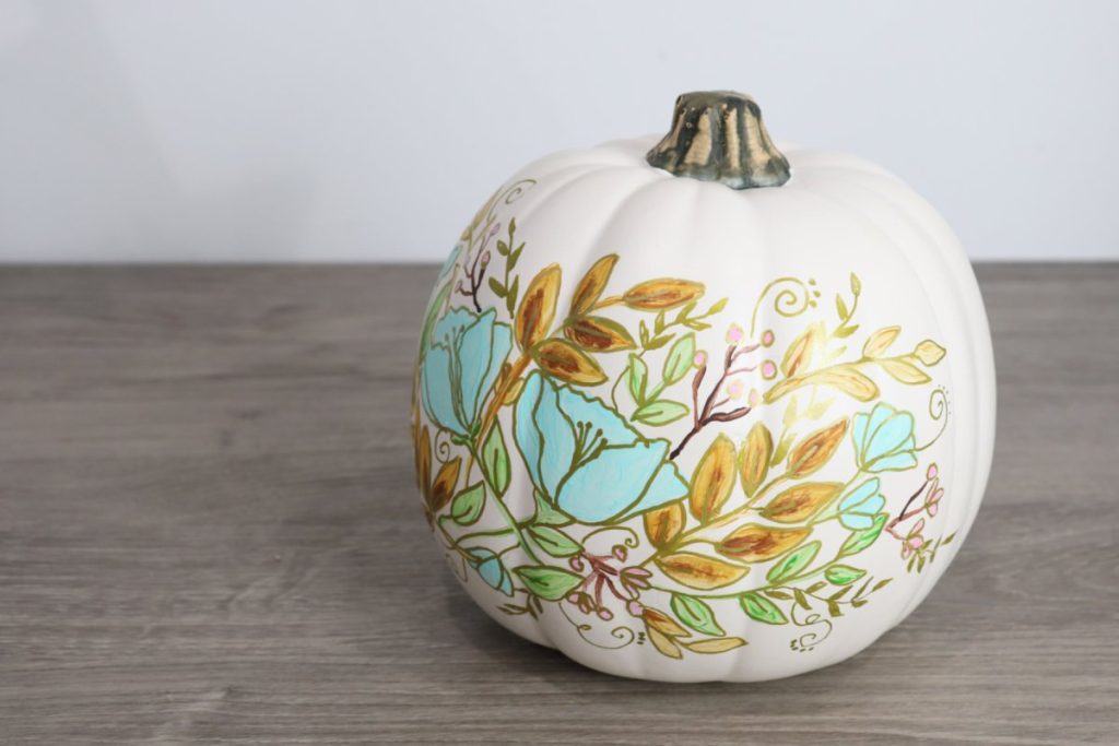 Image contains a white pumpkin with a painted floral design on a wooden desk.