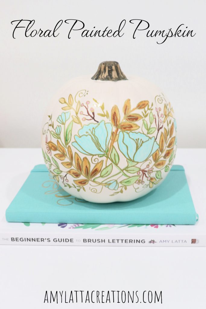 Image contains a white pumpkin decorated with a painted floral design in teal, pink, gold, green, and brown. 