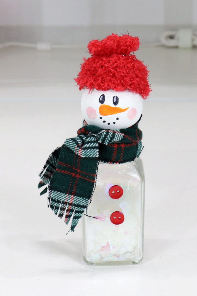 Image contains a salt shaker snowman, made with a shaker, wooden bead, fabric, and paint.