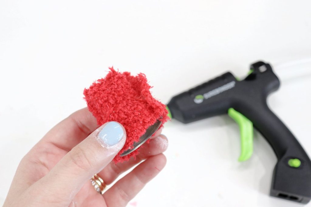Image contains Amy’s hand holding the salt shaker cap wrapped in fuzzy red fabric. A black glue gun sits on a white table in the background.