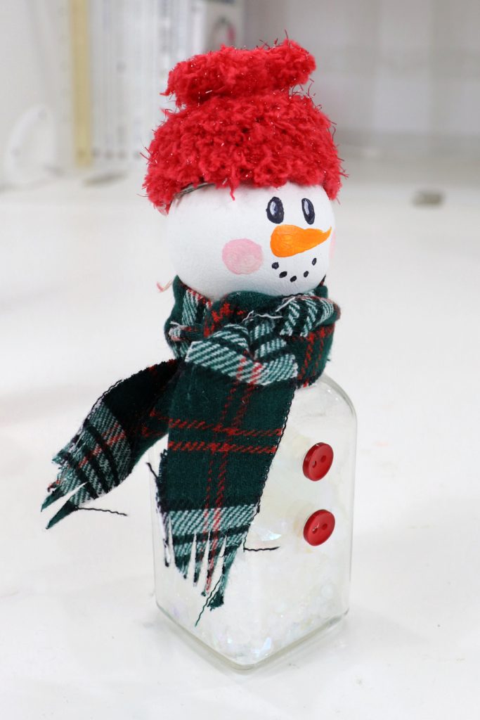 Image contains a snowman made from a salt shaker, a wooden bead, fabric, and buttons.
