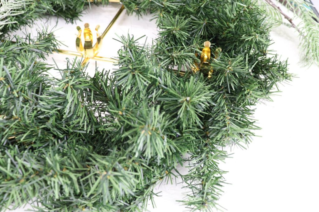 Image contains a faux pine wreath with a gold metal ring and candle holders inside.