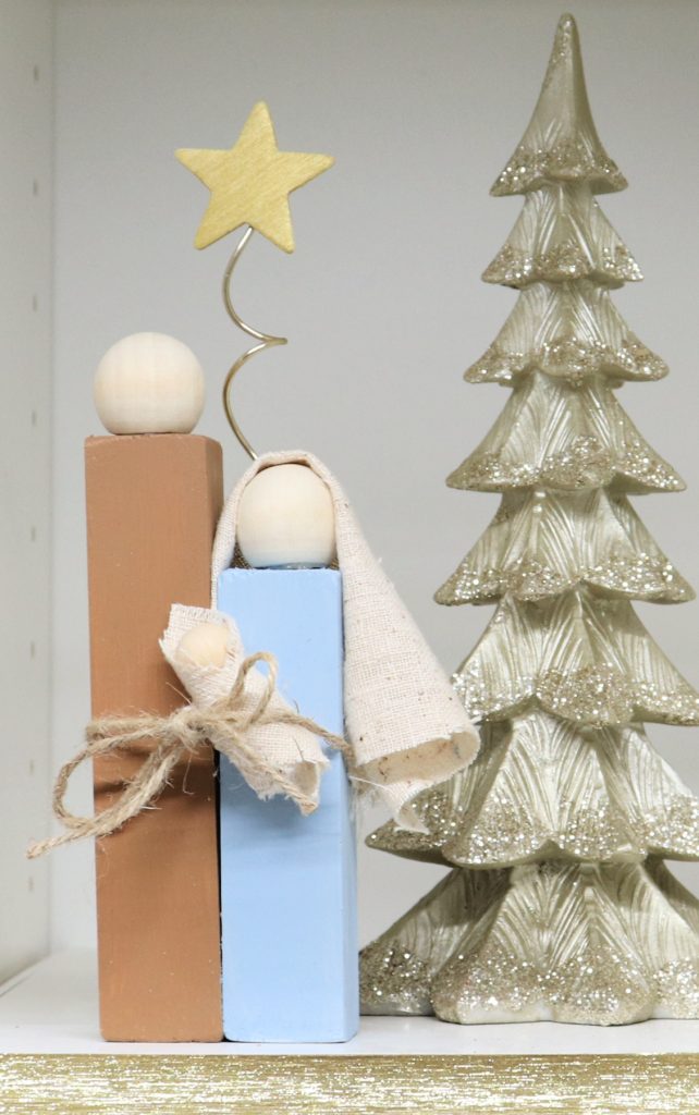 Image contains a wooden block nativity next to a gold tree decoration.