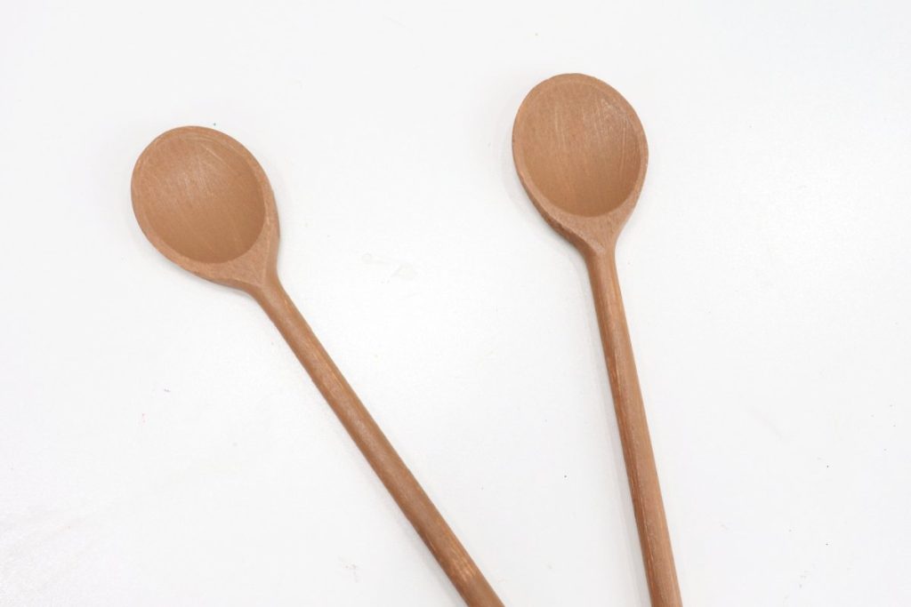 Image contains two wooden spoons painted brown, laying on a white background.