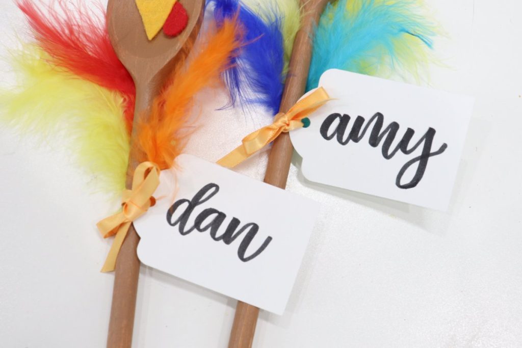 Image contains two white cardstock tags labeled, “amy” and “dan” in black brush script. Each is tied to a spoon handle with gold ribbon.