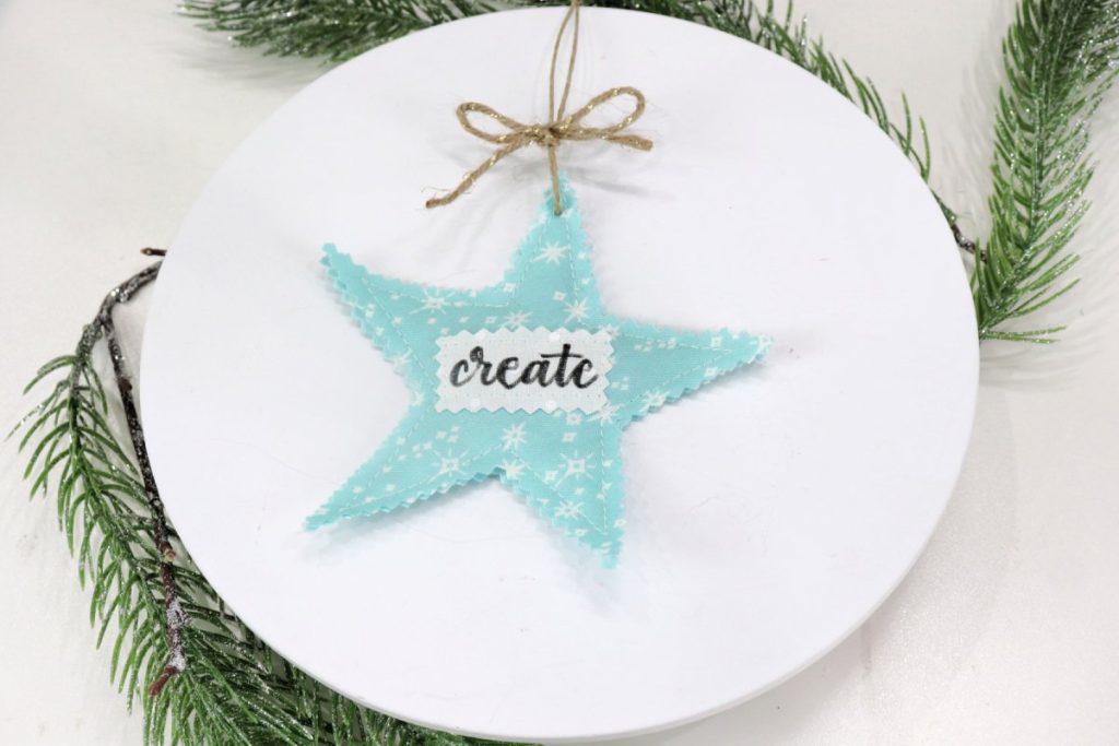 Image contains the finished scrappy star project on a white tabletop with faux pine branches.