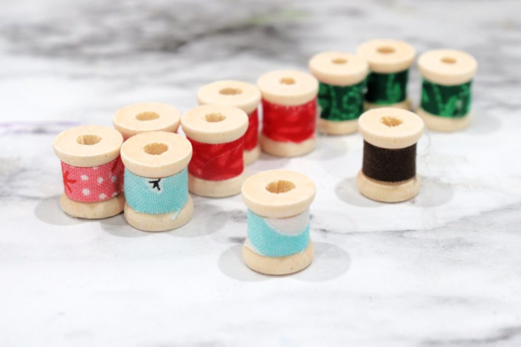Image contains 11 wooden spools covered in assorted colors of fabric, sitting on a marble countertop.