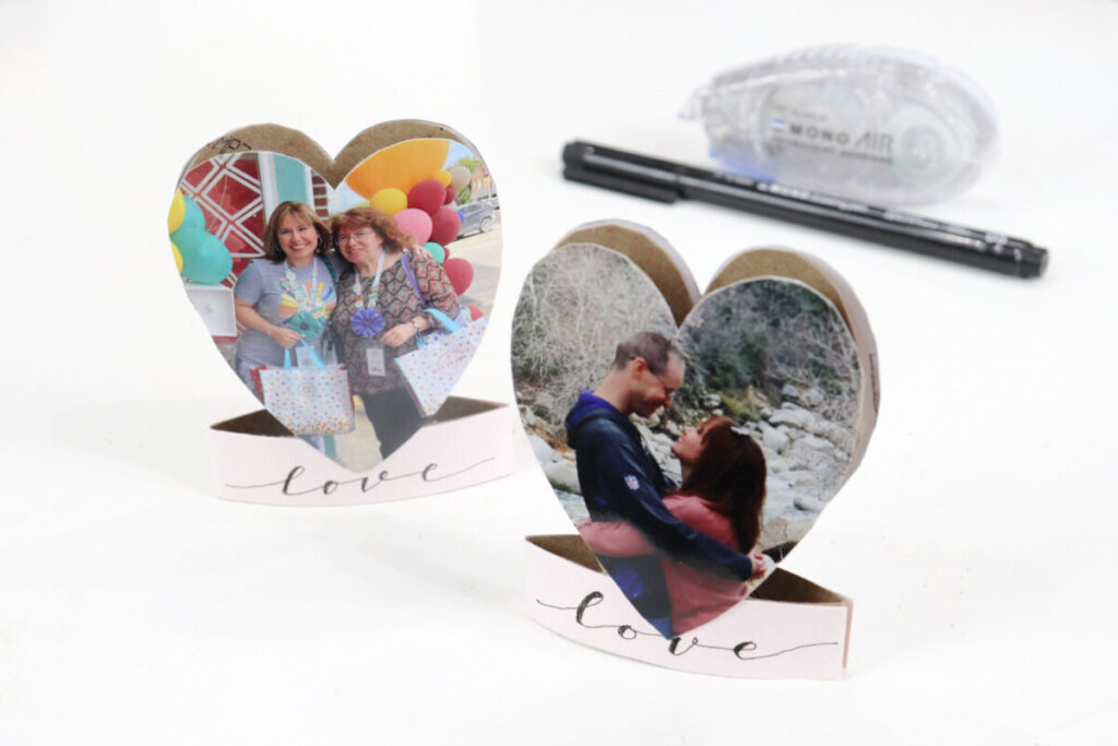 Image contains two heart shaped valentines made from paper rolls, with a photo on each. A MONO Drawing Pen and an adhesive roll sit in the background on a white table.