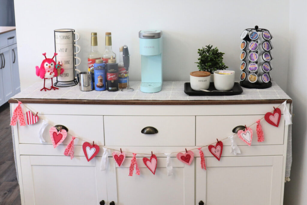 Image contains a coffee bar styled for Valentine's Day with the banner draped across the front. 