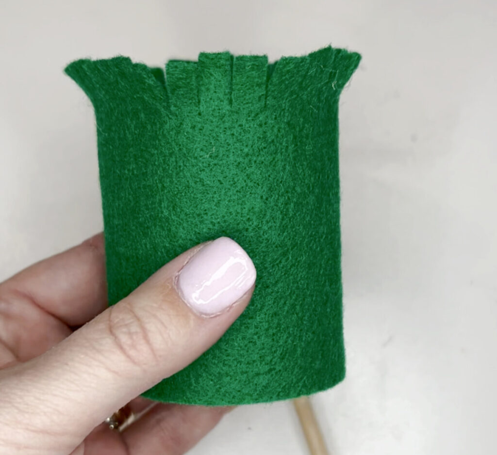 Image contains Amy’s hand holding a paper roll tube covered with green felt that is snipped at the top to look like grass.