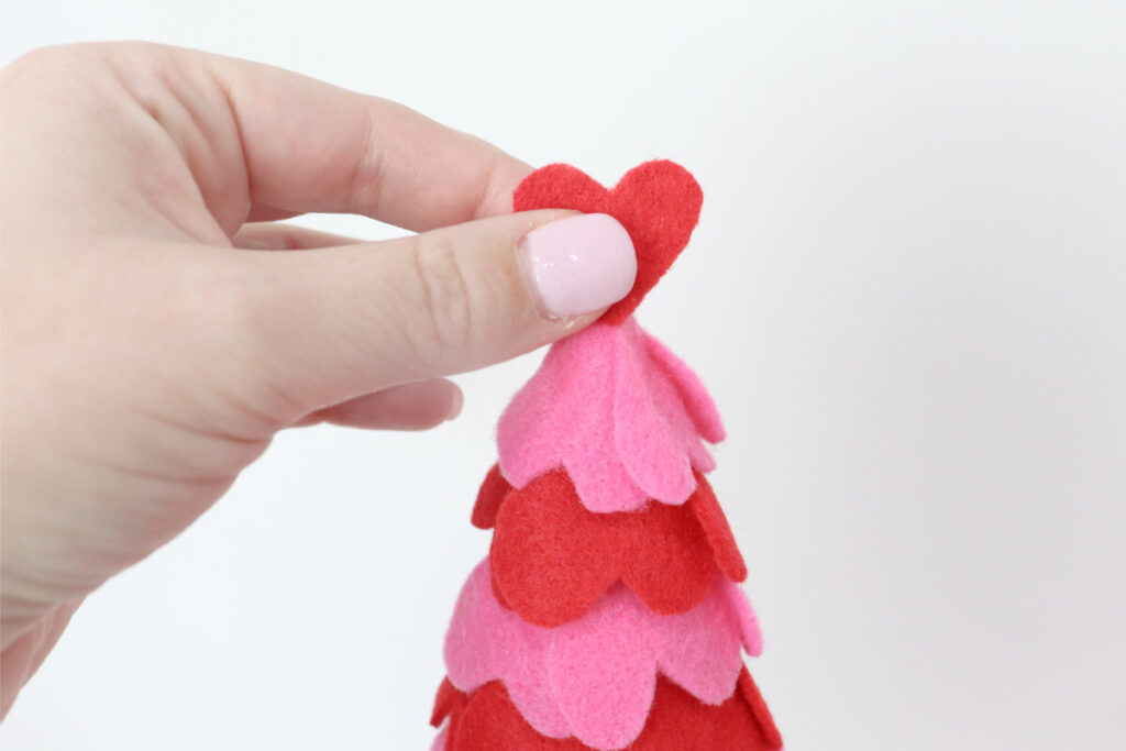 Image contains Amy’s hand placing a red felt heart topper on the felt heart tree.