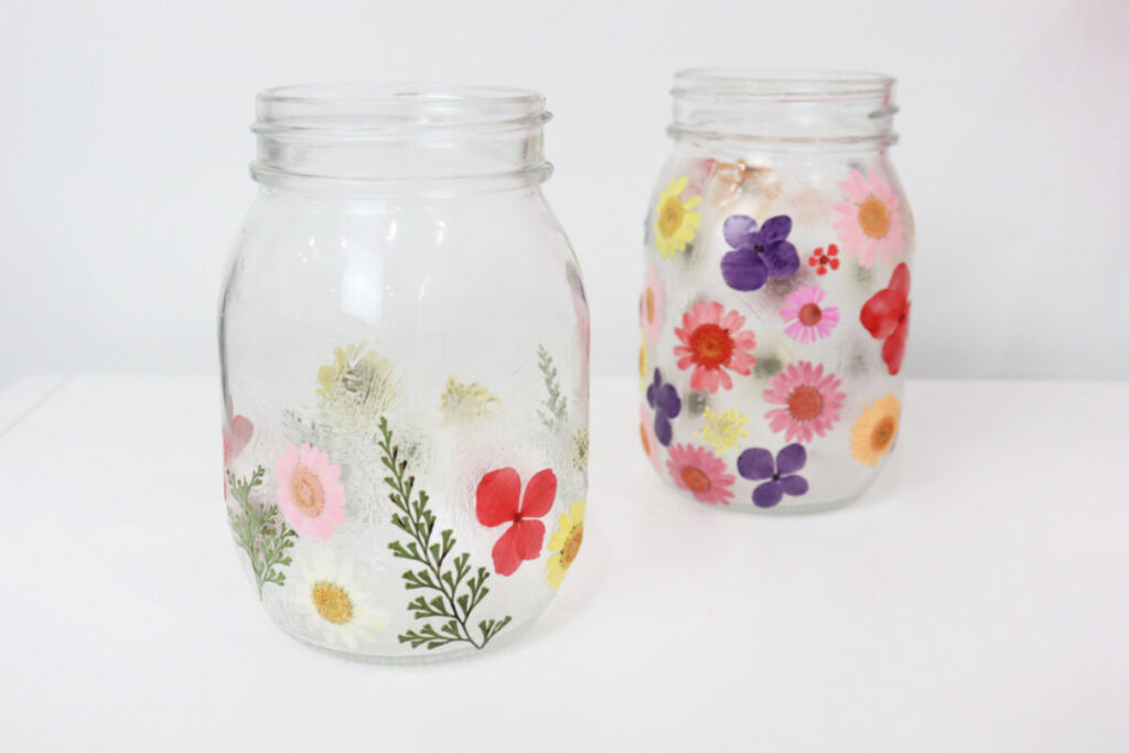 Image contains two mason jars covered with assorted colors and styles of small pressed flowers.