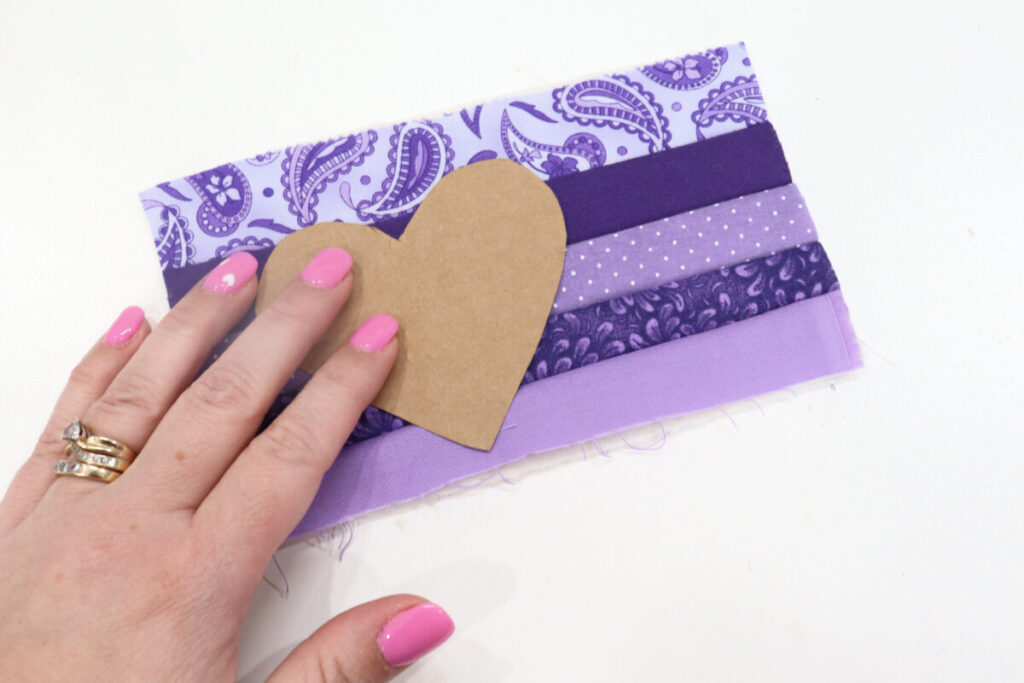 Image contains Amy’s hand holding a heart pattern on top of the sewn fabric strips.