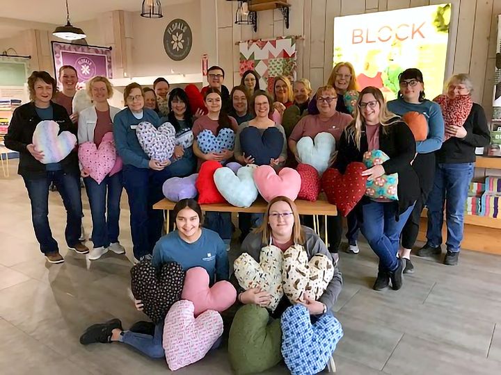 Image contains a group of employees from Missouri Star Quilt Company holding plush heart pillows for donation.