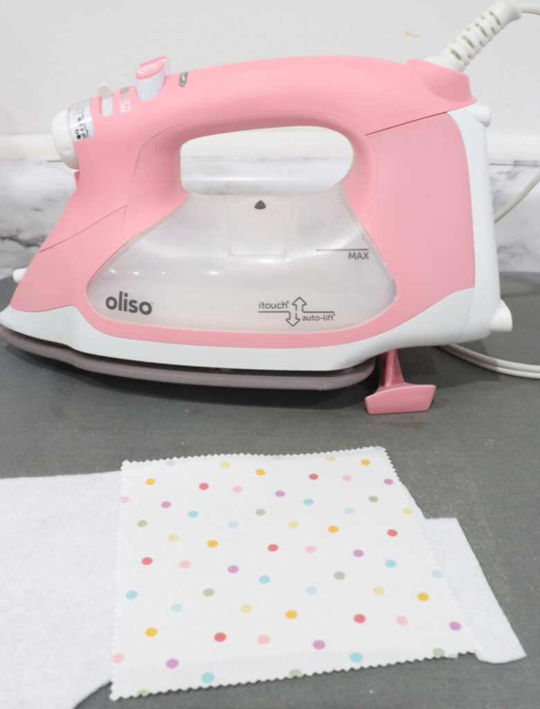 Image contains a pink Oliso iron and a piece of white polka dot fabric ironed to white felt.